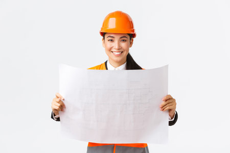 Excited smiling asian female engineer at construction area study blueprints, looking pleased while...