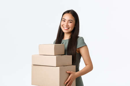 Small business owners, startup and work from home concept. Smiling young store manager, asian businesswoman collect packages, packing orders in boxes and carry them to delivery companyの写真素材