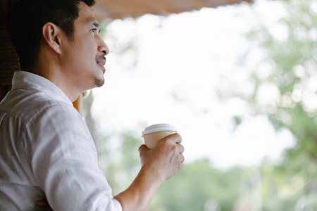Close-up of young man holding coffee to take away at early morning at home, sunlight, blurred...