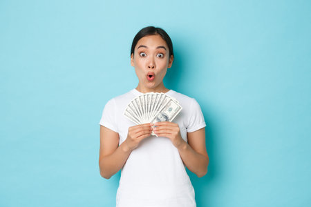 Shopping, money and finance concept. Excited happy asian girl showing cash of dollars and rejoicing,...