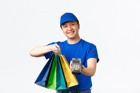 Contactless payment, shopping and home delivery concept. Smiling pleasant asian courier in blue...