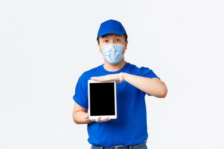 Online shopping, covid-19, preventing virus and delivery concept. Surprised asian courier in medical...