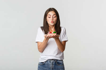 Excited and dreamy cute birthday girl making wish on b-day cake, blowing candleの写真素材
