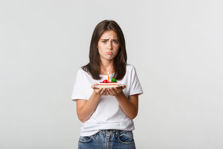 Miserable birthday girl looking sad, holding b-day cake with candle