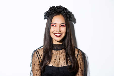 Close-up of beautiful elegant woman in witch costume and gothic makeup, smiling pleased while looking at upper left corner, celebrating halloweenの写真素材