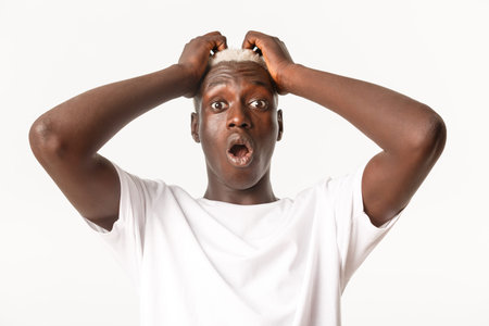 Close-up of ambushed and shocked african-american blond guy, gasping and looking startled, holding...