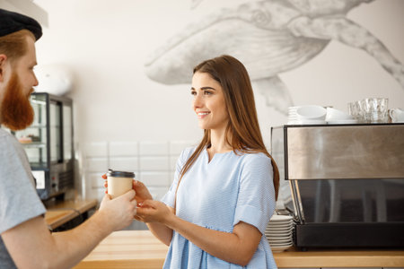 Coffee Business Concept - young smart bearded bartender enjoy talking and giving take away cup of...