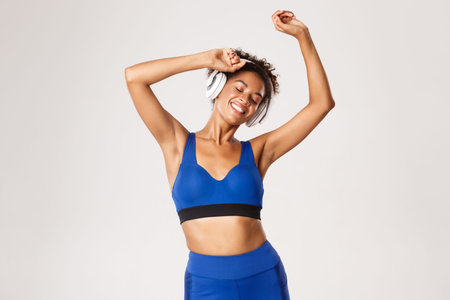 Sport and lifestyle concept. Happy fit african-american woman dancing, smiling with eyes closed,...