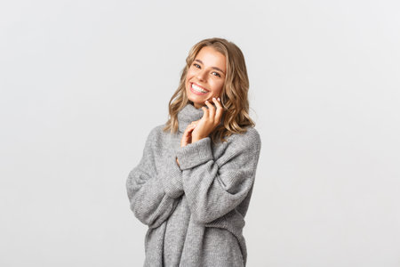 Portrait of tender smiling woman, looking happy and laughing, gently touching face, standing over...