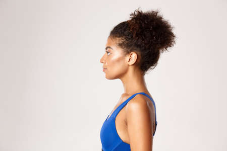 Concept of workout and sport. Profile of young athletic girl in blue sports bra, looking left, standing against white backgroundの写真素材