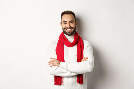Christmas holidays and celebration concept. Handsome bearded man in sweater celebrating new year, wearing red scarf and smiling, standing over white backgroundの写真素材