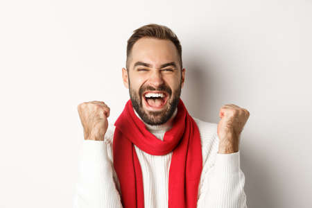 Christmas holidays. Close-up of happy guy winner, celebrating victory, raising hands up and shouting yes for joy, achieve goal, white backgroundの写真素材