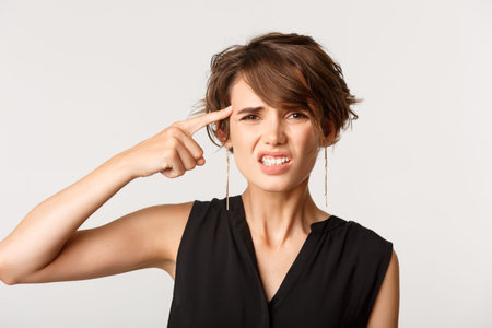 Close-up of annoyed woman scolding person, pointing finger at head and looking frustrated, standing...