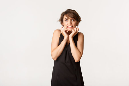 Image of scared timid girl in black dress, looking frightened and trembling from fear, standing over...