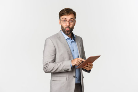 Image of surprised businessman with beard, wearing grey suit and glasses, saying wow and looking...