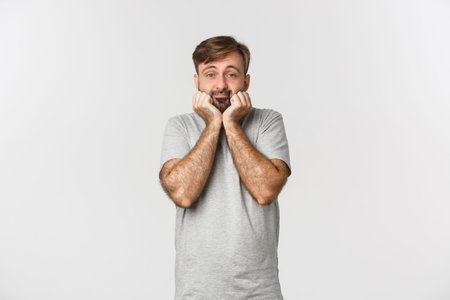 Portrait of cute and silly adult man with beard, leaning on palm and looking at camera silly,...
