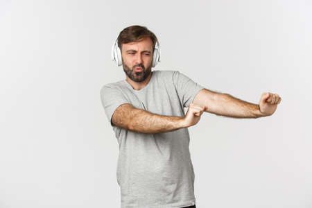Portrait of happy guy dancing to music in headphones, standing over white backgroundの写真素材