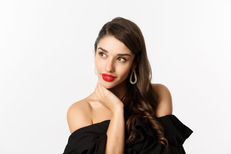 Fashion and beauty concept. Elegant woman with earrings and black dress, looking left sensual,...