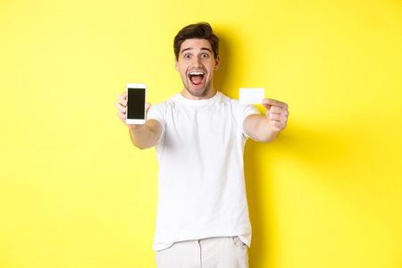 Handsome caucasian man showing smartphone screen and credit card, concept of mobile banking and...