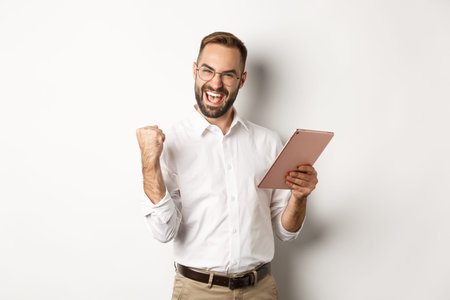 Successful businessman rejoicing on winning online, reading on digital tablet and making fist pump,...