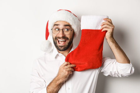 Close-up of happy man celebrating christmas, receive gifts in xmas sock and looking excited, wearing...