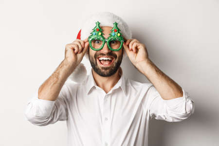 Close-up of happy man celebrating christmas holidays, wearing party glasses and santa hat, enjoying New Year, white backgroundの写真素材
