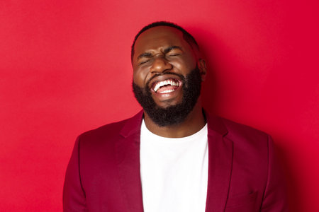 Close-up of happy and carefree Black man having fun, laughing and smiling, standing in blazer...