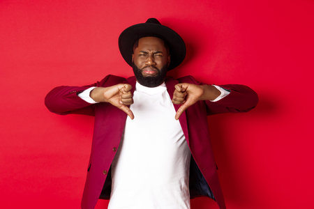 Disappointed Black man leave negative feedback, showing thumb down and grimacing from dislike and...