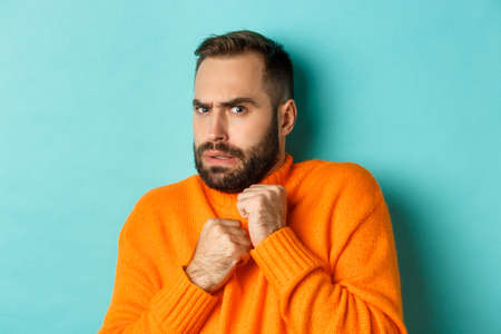 Close-up of scared bearded man looking startled and displeased, jumping from fear, standing over light blue backgroundの写真素材