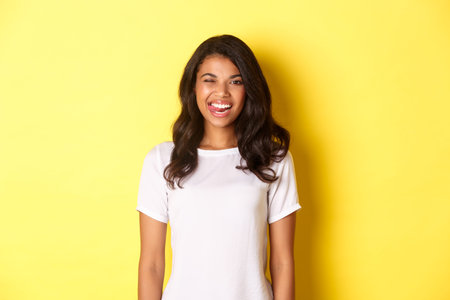 Image of carefree african-american girl in white t-shirt, showing tongue, smiling and winking happy,...