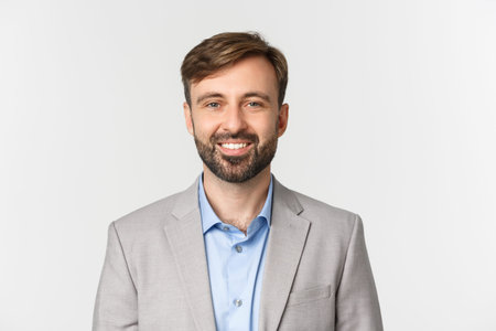 Close-up of confident bearded businessman in gray suit, smiling self-assured, standing over white...