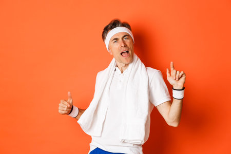 Image of happy and carefree middle-aged fitness guy, dancing after workout, holding towel over neck,...