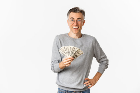 Portrait of amazed middle-aged man in glasses and gray sweater, holding money and smiling cheerful,...