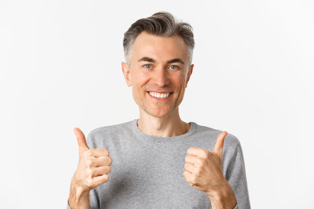 Close-up of cheerful middle-aged man, smiling happy and satisfied, showing thumbs-up, expressing...