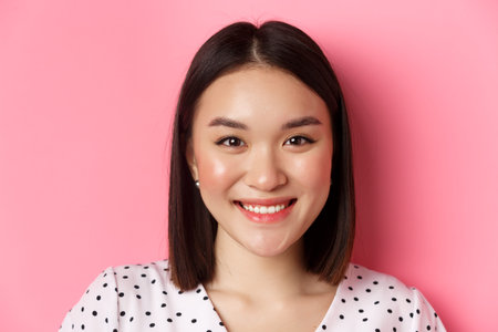 Beauty and lifestyle concept. Headshot of beautiful asian woman smiling, looking at camera happy and...