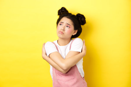 Sad lonely asian girl looking aside with upset and gloomy face, hugging herself, dreaming of love...