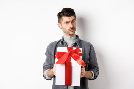 Surprised young man look with disbelief and hold surprise gift, raising eyebrow doubtful, being...