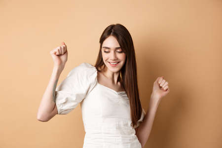 Carefree woman dancing and having fun, close eyes and smiling, standing on beige backgroundの写真素材