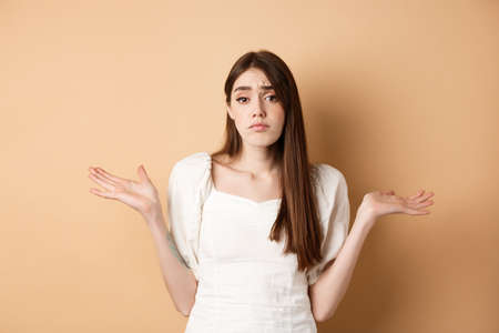I dont know. Clueless sad girl shrugging shoulders and looking unaware, have nothing to say, standing on beige backgroundの写真素材