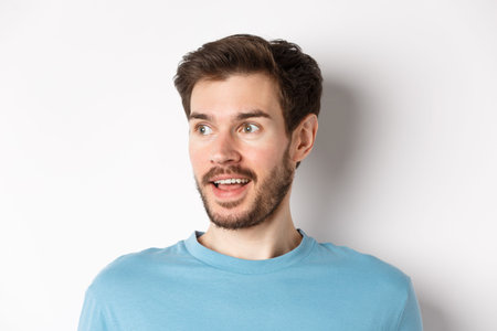 Close-up of surprised and excited bearded man, looking left with opened mouth and amazed face,...