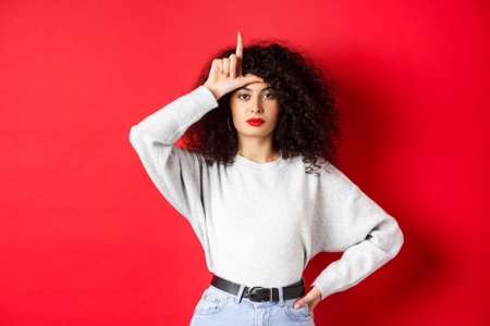 Confident european woman with curly hair, mocking lost team, showing loser gesture and staring...