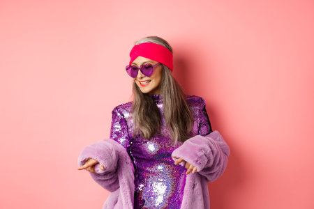 Fashionable asian senior woman dancing disco, wearing glittering shiny dress and heart-shaped...