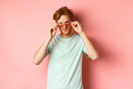 Handsome redhead man in summer sunglasses looking sassy at camera, standing over pink backgroundの写真素材