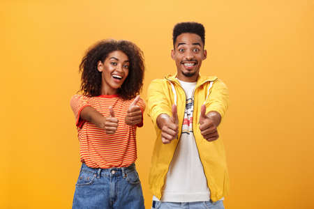Two friends like perfect and awesome plan. Portrait of joyful friendly-looking optimistic african american female and male showing thumbs up in approval and agreement gesture smiling broadlyの写真素材
