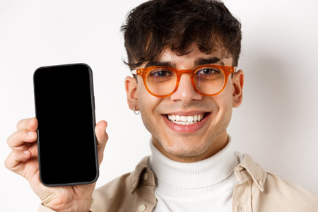 Face of handsome smiling guy in glasses showing empty smartphone scree, white background