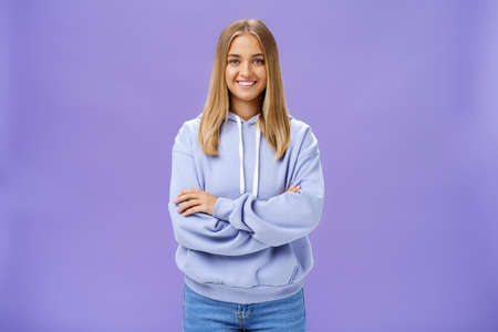 Portrait of charming charismatic european woman with tanned skin in trendy over-sized hoodie crossing hands against chest smiling broadly at camera standing self-assured against purple backgroundの写真素材