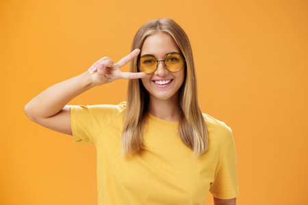 Cute optimistic and friendly young caucasian woman with fair hair in yellow t-shirt and sunglasses...