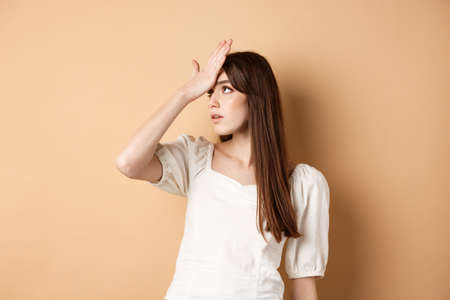 Girl rolling her eyes and slap forehead annoyed, bothered by something stupid or lame, making face palm on beige backgroundの写真素材