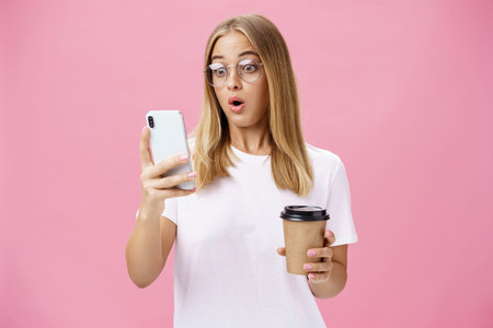Woman drinking coffee being shocked by received message reacting on stunning news folding lips...