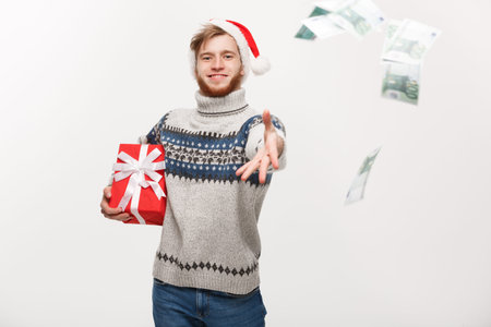 Holiday Concept - Young beard man holding christmas gift and throwing money to camera.